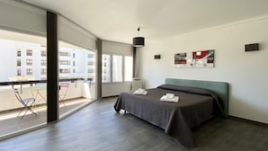 Et moderne hotelværelse med en stor seng, udsigt over byen og en balkon med stole.