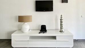 Et hvidt multimøbel med fjernsyn, lampe, fjernbetjening og en dekorativ fyrtårn.