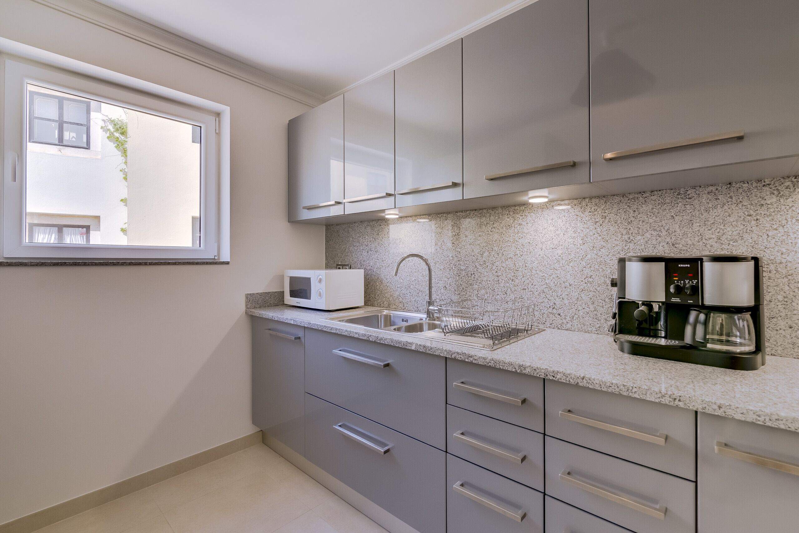 Une cuisine moderne dotée d’un plan de travail en granit, d’appareils électroménagers en acier inoxydable et d’une fenêtre offrant une vue sur un bâtiment à l’extérieur.
