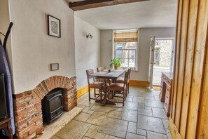 Une pièce avec une cheminée, une table à manger avec des chaises, une fenêtre avec des stores et une vue sur l’extérieur.