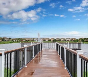 A wooden deck with railings leading to a body of water, surrounded by houses. - Newly furnished resort home with private pool, hot tub and games room - Windsor at Westside (Kissimmee)