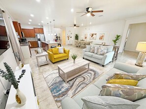 A modern living room with a yellow sofa, a grey sofa, and a coffee table. There is a dining area with a table and chairs. - Newly furnished resort home with private pool, hot tub and games room - Windsor at Westside (Kissimmee)
