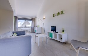 Ein modernes Wohnzimmer mit einer Couch, einem Couchtisch, einem Fernseher und einer weißen Kommode mit grünen Akzenten.