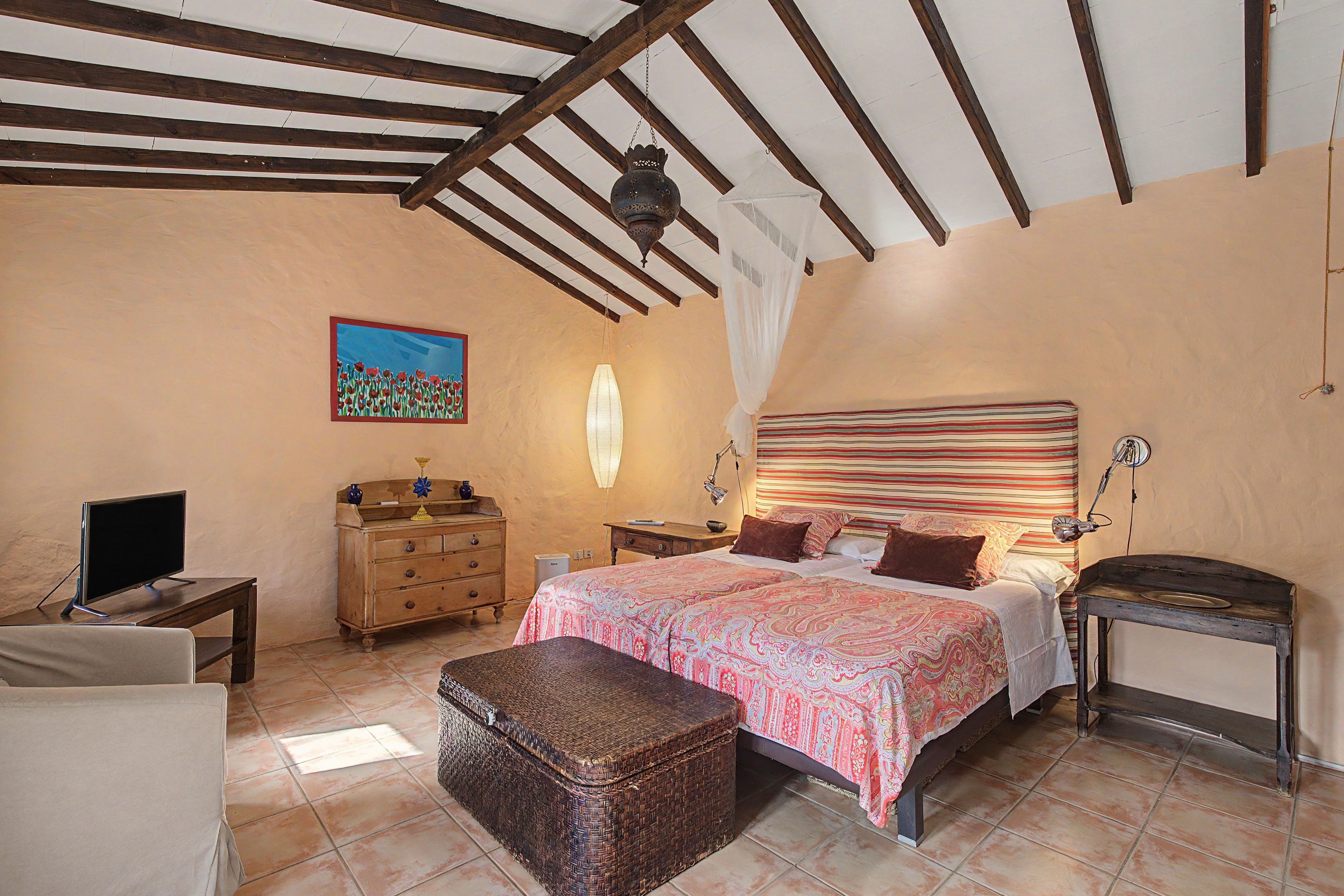 Ein Schlafzimmer mit einem großen Bett, einem Schminktisch, einem Sessel, einem kleinen Tisch und einer Wanddekoration.