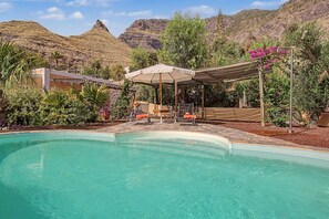 A swimming pool with a pergola and chairs, surrounded by lush vegetation and a mountain backdrop. - El Patio de Agaete Country House with Sea Views, Private Pool and Wi-Fi (Agaete)