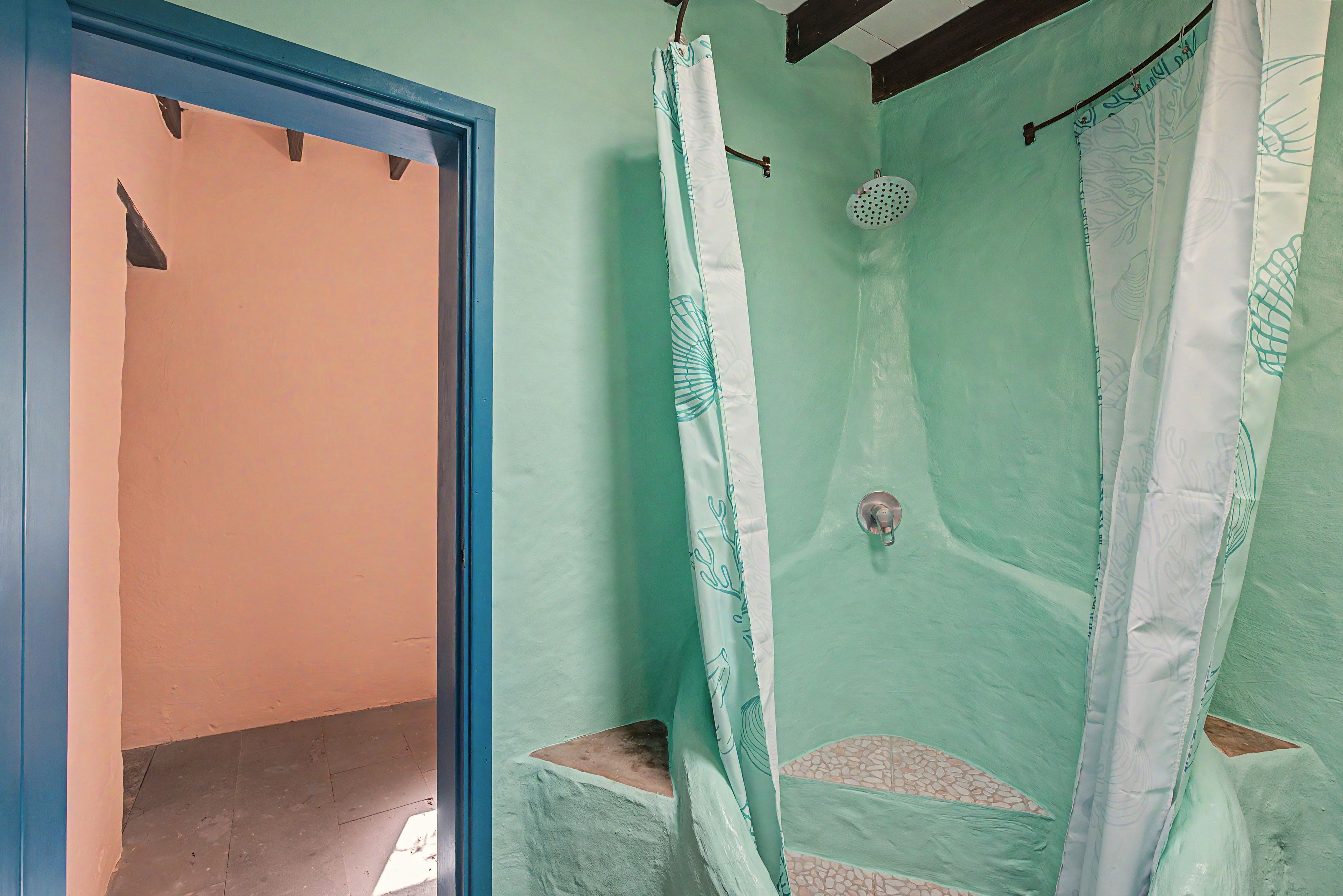 Une salle de bain avec une douche, une porte donnant sur une autre pièce et un sol carrelé.