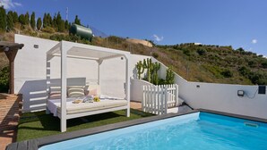 A poolside area with a white bed and a white fence.