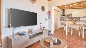 A modern kitchen with a flat-screen TV, wooden ceiling, white cabinets, and a dining area with a table and chairs.