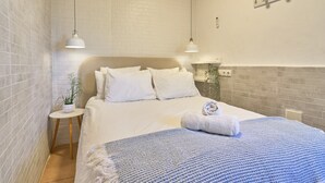 A bedroom with a bed, two pendant lights, a small side table with a plant, and a wall-mounted light fixture.