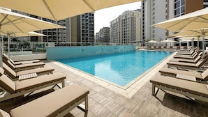 A swimming pool with lounge chairs and umbrellas, surrounded by high-rise buildings. - New Studio w/ Balcony & Pool | Riviera Beachfront (Dubai)
