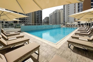 Ein Pool mit Liegestühlen und Sonnenschirmen, umgeben von Hochhäusern.