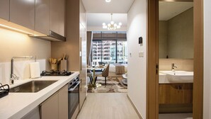 A modern kitchen with a built-in stove, a sink, and a dining area with a table and chairs. - New Studio w/ Balcony & Pool | Riviera Beachfront (Dubai)