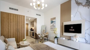 A modern hotel room with a bed, sofa, TV, dining area, and kitchen in the background. - New Studio w/ Balcony & Pool | Riviera Beachfront (Dubai)