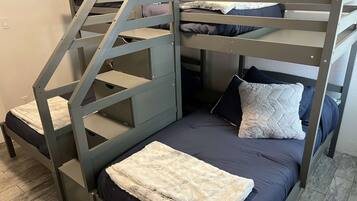 Uma cama beliche com escada, um cobertor branco e fofo, e roupa de cama azul escura.