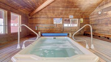 Uma cabana de madeira com hidromassagem, piso de madeira e teto com vigas de madeira. Há placas indicando capacidade do spa para 8 pessoas e aviso de salva-vidas de serviço.