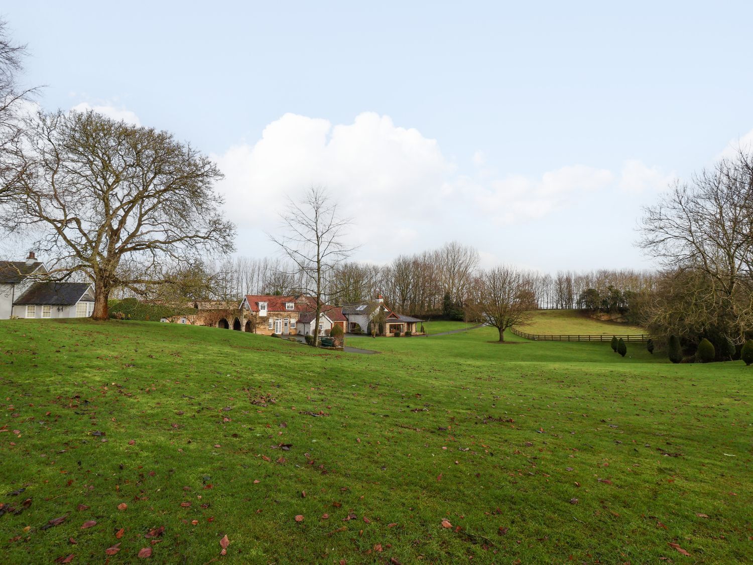 A rural landscape with a large house, a smaller building, and a grassy field.