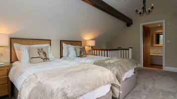 A bedroom with two beds, a chandelier, a wooden ceiling beam, and a bathroom visible through an open door.