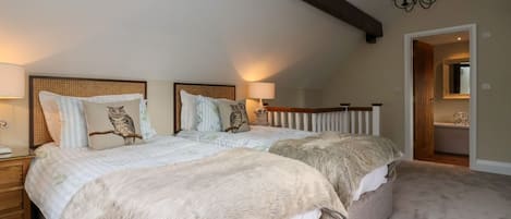 Un dormitorio con dos camas, un candelabro, una viga de techo de madera y un baño visible a través de una puerta abierta.