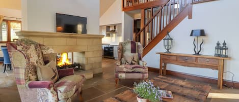 Un salón espacioso con chimenea, una escalera de madera y un comedor con una mesa rústica.