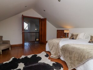 Une chambre avec un plafond en pente, un lit recouvert d’une couette blanche, une chaise en bois, un tapis en peau de vache et une porte donnant sur un balcon.