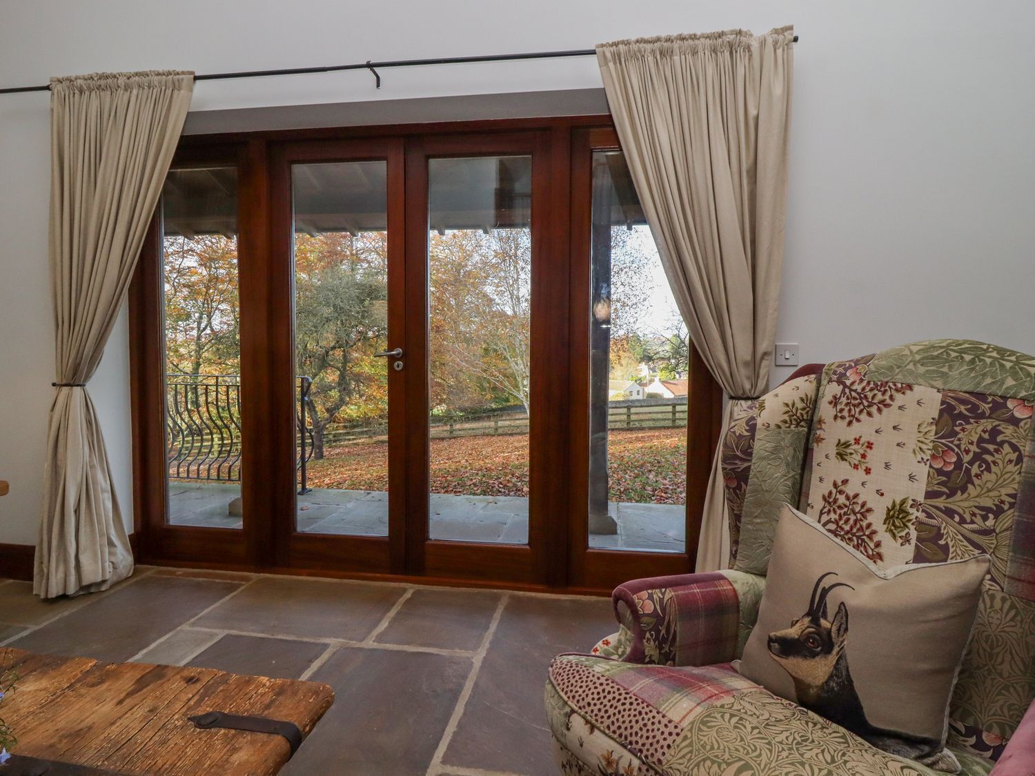 Una habitación con piso de piedra, una puerta de madera que da a un espacio exterior y un sillón con estampado.