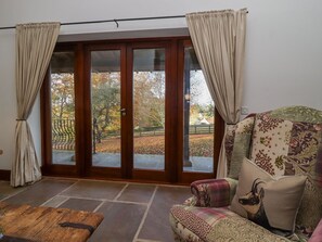 A room with a stone floor, a wooden door leading to an outdoor area, and a patterned armchair.