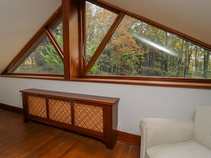 A room with a large triangular window, a wooden console table, and a beige armchair. - Sandy Gate (Knaresborough)