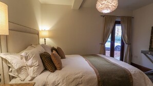Un dormitorio con cama, almohadas, lámpara, lámpara colgante y ventana con cortinas.