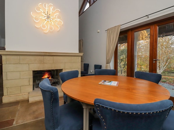 A room with a fireplace, a round wooden table, and blue upholstered chairs. - Sandy Gate (Knaresborough)