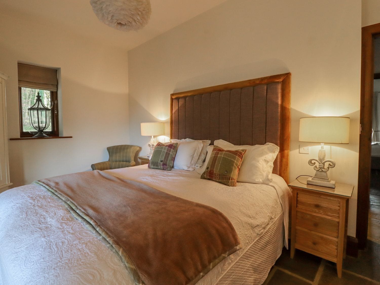 A bedroom with a large bed, two bedside tables with lamps, a chair, a window with a view, and a wooden headboard.