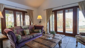 Una habitación acogedora con un sofá morado, una mesa de centro de madera y ventanas grandes con cortinas.