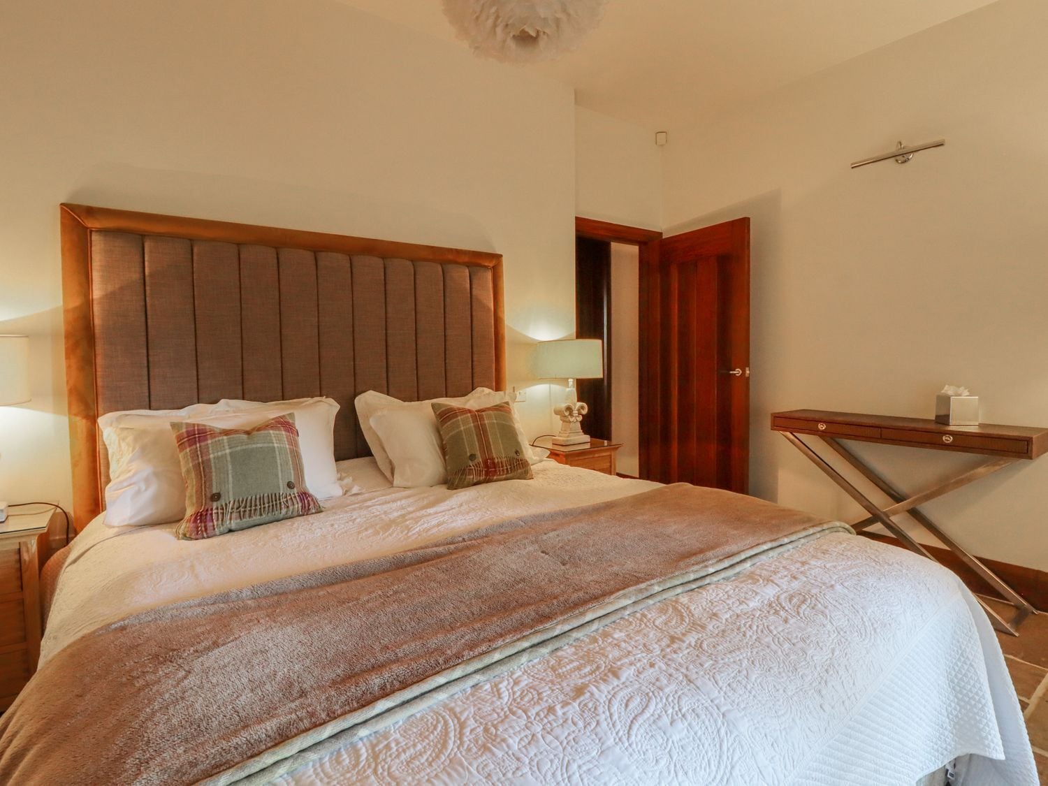A neatly made bed with a wooden headboard, a bedside table with a lamp, and a small wooden shelf with a tissue box.