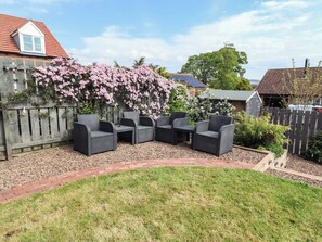 A patio with outdoor furniture, a wooden fence, and flowering plants. - 26 Field Court (Wooler)
