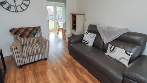 A living room with a striped armchair, a brown leather sofa, and a large wall clock. - 26 Field Court (Wooler)