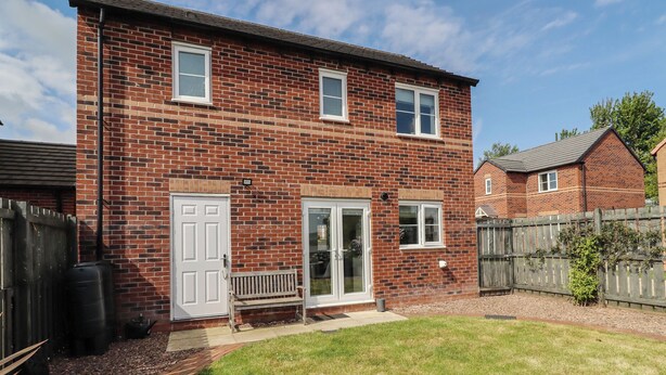 A two-story brick house with a front door, two windows, a bench, and a small garden. - 26 Field Court (Wooler)