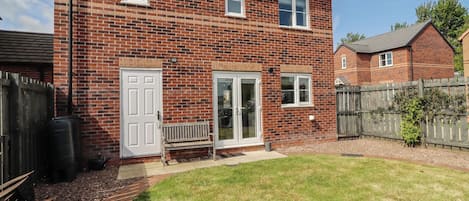 A two-story brick house with a front door, two windows, a bench, and a small garden.