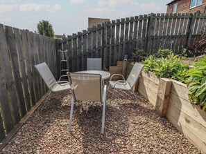 A patio with a table and chairs, surrounded by a wooden fence and plants. - 26 Field Court (Wooler)