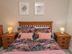 A bedroom with a wooden headboard, floral bedding, two bedside lamps, and two framed artworks on the wall. - 26 Field Court (Wooler)