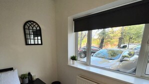 Un dormitorio con cama, ventana que da a coches aparcados, radiador y una planta pequeña en el alféizar.