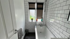 Un baño con paredes de azulejos blancos, una bañera, una ventana con vistas y un perchero para toallas.