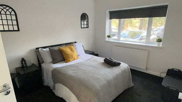 Un dormitorio con cama, ventana, radiador y una planta pequeña.
