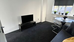 Una sala moderna con un televisor de pantalla plana, un sofá, una mesa de centro y una ventana con persianas.