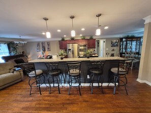 A modern kitchen with a central island, bar stools, stainless steel appliances, and pendant lighting.