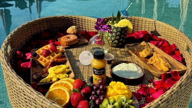 A wicker basket filled with fruits, a waffle, and a drink, placed on a poolside table. - The LaPearla Experience - A Hidden Gem (Riverdale)