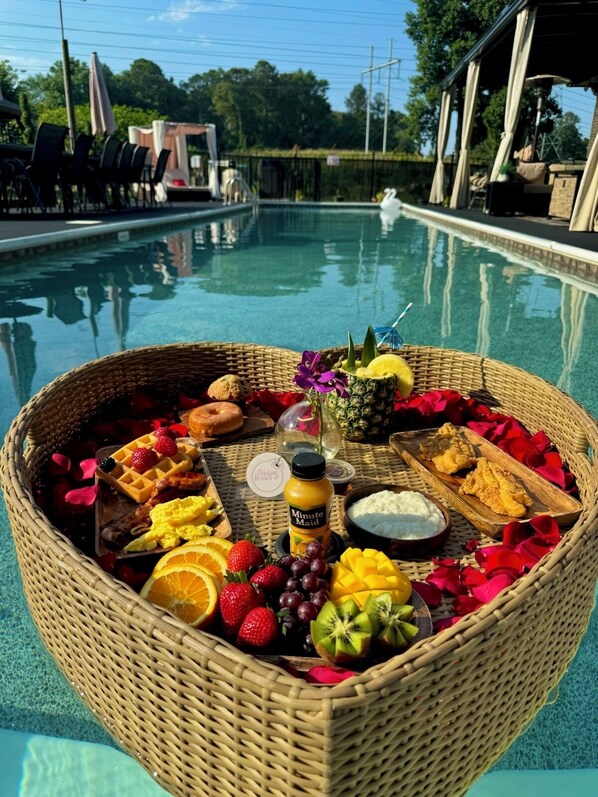 A wicker basket filled with fruits, a waffle, and a drink, placed on a poolside table.