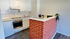 Moderni keittiö, jossa on valkoiset kaapit, tiiliverhoiltu seinä, sisäänrakennettu uuni ja kahvinkeitin.