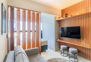 Una sala de estar moderna con un sofá, televisión y dos taburetes de bar.