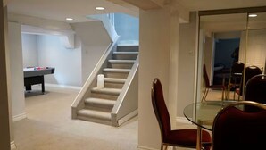 Una habitación con una mesa de vidrio, sillas rojas, una escalera y una mesa de billar.