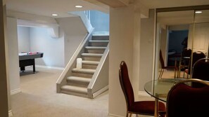 A room with a glass table, red chairs, a staircase, and a pool table.