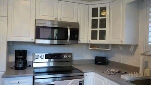 Una cocina con gabinetes blancos, horno de acero inoxidable, microondas y tostadora.